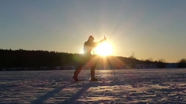 Lyžař jede lyže na zamrzlém jezeře při západu slunce v pomalém pohybu. — Stock video