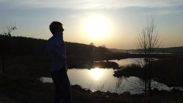Junger Mann tanzt Disco-Stil mit Ohrhörern in den Ohren bei eindrucksvollem Sonnenuntergang im Freien in einem frühen Frühling — Stockvideo