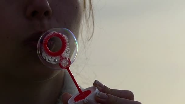 Menina está criando bolhas de sabão com uma varinha de sabão vermelho de uma forma engraçada em câmera lenta . — Vídeo de Stock