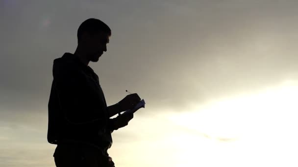 Silhouette dell'uomo che scrive qualcosa nel suo taccuino al tramonto . — Video Stock