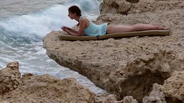 Mädchen ruht auf dem Stein über dem stürmischen Ozean in Zeitlupe. — Stockvideo