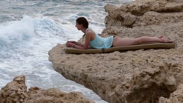 Attraktive junge Frau bräunt sich im Herbst auf einer hölzernen Liege am steinigen Strand des Roten Meeres. — Stockvideo