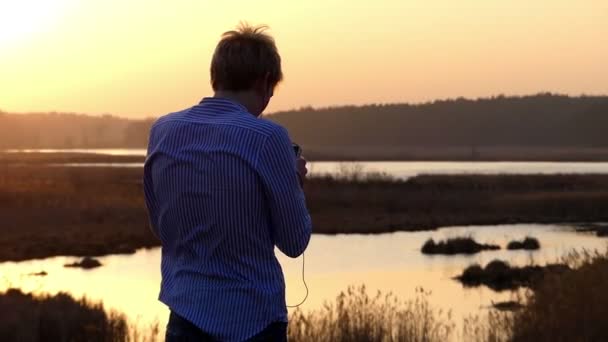 Muž, který stojí při západu slunce na les a poslech hudby. Pohled zezadu. — Stock video