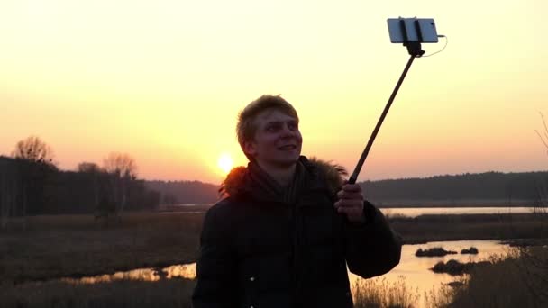 Mann macht Selfie bei Sonnenuntergang mit Selfie-Stick. — Stockvideo