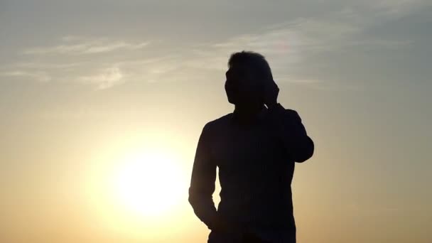 Junger Mann steckt sich Ohrhörer in die Ohren, tanzt und hebt abwechselnd die Hände mit einem herrlichen Sonnenuntergang im Hintergrund im zeitigen Frühling — Stockvideo
