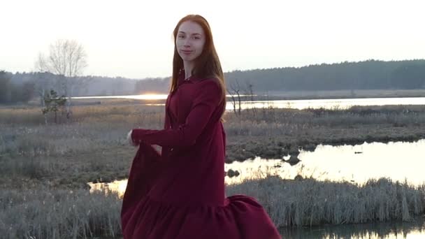 Beau modèle en robe rouge torsadant et dansant au ralenti au coucher du soleil . — Video