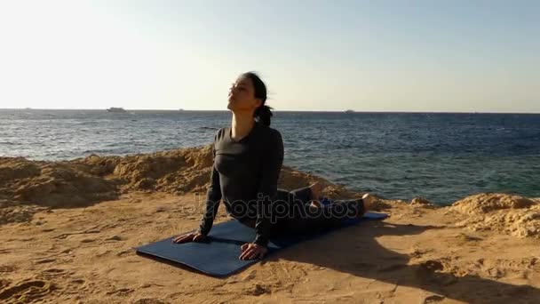 Lány csinál jóga a köves tengerparton naplementekor. — Stock videók