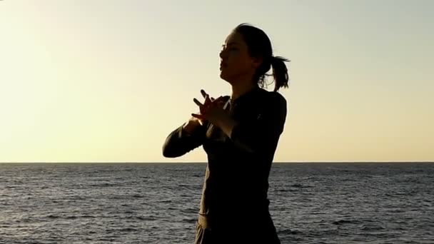 Chica hace ejercicio para una espalda sana en cámara lenta en la playa pedregosa al atardecer . — Vídeos de Stock