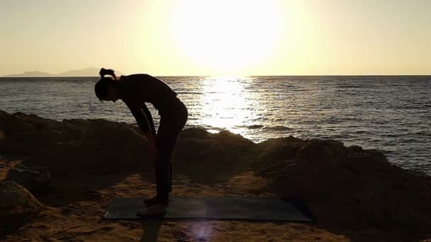 Meisje maakt oefening voor Healthy Back in Slow Motion op het stenige strand bij zonsondergang. — Stockvideo