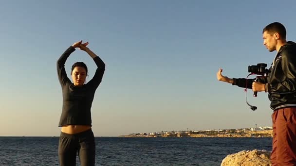 Uomo con Steadycam che lavora al tramonto sulla spiaggia. egli Record modello e raccontare a lei alcune istruzioni . — Video Stock