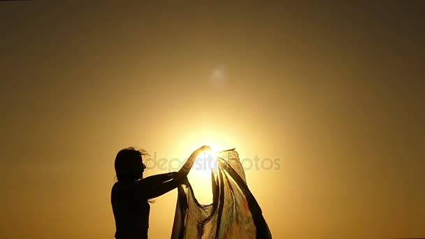 Silhouette di una giovane donna, in piedi su una costa rocciosa e mantenendo un pezzo di panno trasparente sul vento in un bel tramonto in Egitto a Slo-Mo — Video Stock