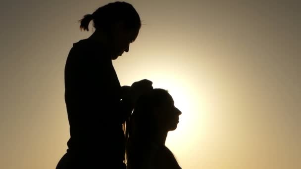 座っていると、夕暮れ時の順序で髪を入れて 2 つの若い女性のシルエット. — ストック動画
