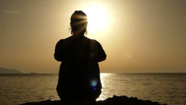 Menina sentada na pedra da praia ao pôr do sol e admirar a paisagem . — Vídeo de Stock