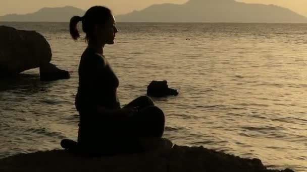 Κορίτσι καθαρισμό αύρας στο ηλιοβασίλεμα που κάθεται στην πέτρα της παραλίας σε αργή κίνηση. — Αρχείο Βίντεο