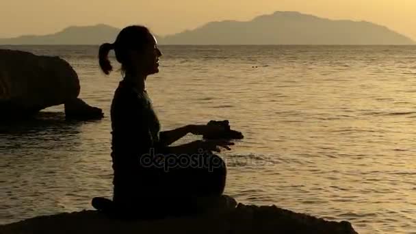 Смешная девушка очищает свою ауру на закате, сидя на камне . — стоковое видео