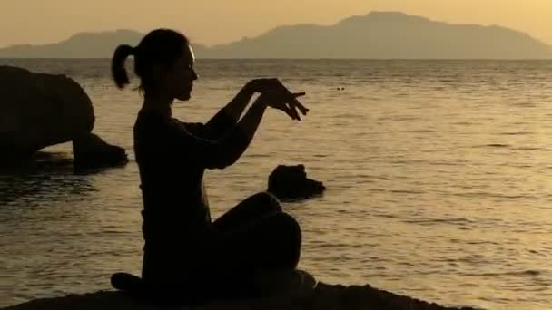 Dziewczyna siedzi na kamieniu o zachodzie słońca i praca z energia Chi. — Wideo stockowe