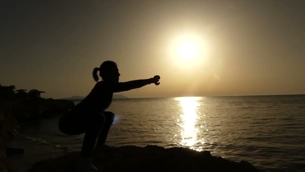 Úžasné dřepy žena sportovců při západu slunce v pomalém pohybu na pobřeží moře — Stock video