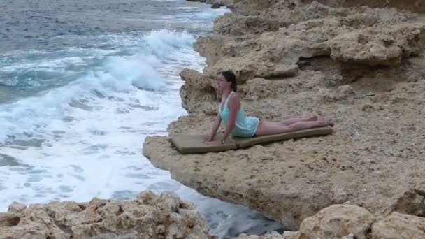 Ung kvinna gör en Yoga Asana kallad 'cobra' på en stenig Seabeach i Egypten på dagtid under hösten — Stockvideo