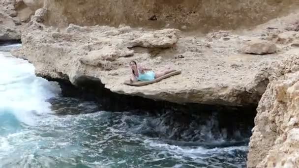Mädchen liegt auf der Klippe über dem Meer und winkt mit der Hand. — Stockvideo