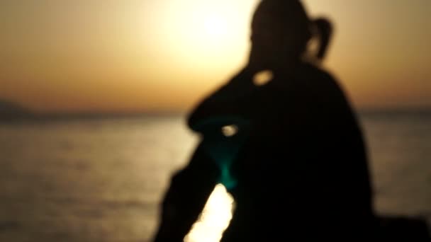 Kız gün batımında sahilde oturan ve telefon kullanarak odak dışı. — Stok video