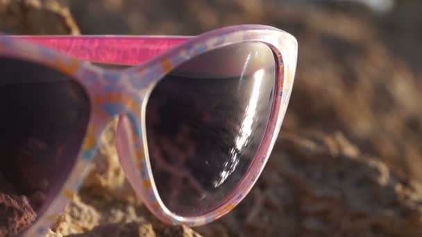 Nahaufnahme einer Sonnenbrille mit Spiegelung des schönen Sonnenuntergangs am Meer. — Stockvideo