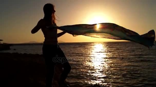 Silhouette eines Mädchens und der Wind, der bei Sonnenuntergang durch den Schal rauscht. — Stockvideo