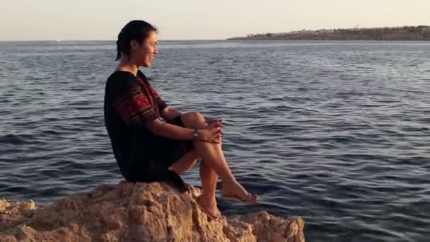 여 자가 앉아서 우크라이나어 드레스에서 돌 해변에 돌에 웃 고. — 비디오