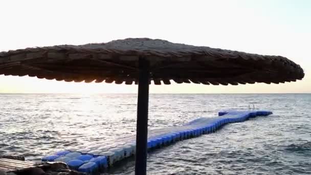 Paraplu op het strand van het Hotel in de stralen van de zon bij zonsondergang. — Stockvideo