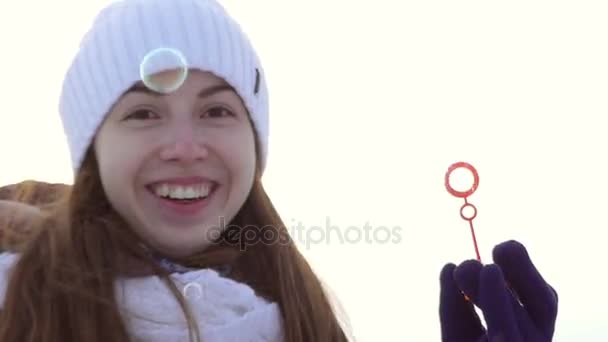 Mladá dívka v zimě oblečení Holdes v ruce hůlku pro mýdlové bubliny a smích. — Stock video