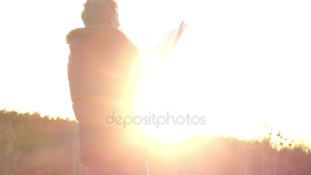 Hezký chlapec stojí s knihou venku, osvětlené paprsky zapadajícího slunce, zadní pohled v pomalém pohybu — Stock video