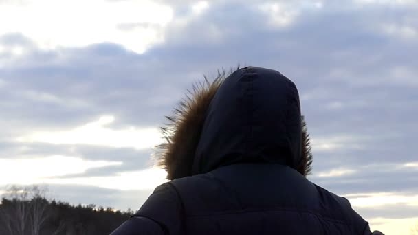 L'uomo incappucciato sta con la schiena alla macchina fotografica sullo sfondo della natura durante il tramonto in slow motion — Video Stock