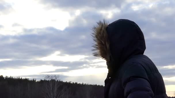 Un uomo con un cappuccio bancarelle laterali su uno sfondo di natura durante un tramonto in slow motion — Video Stock