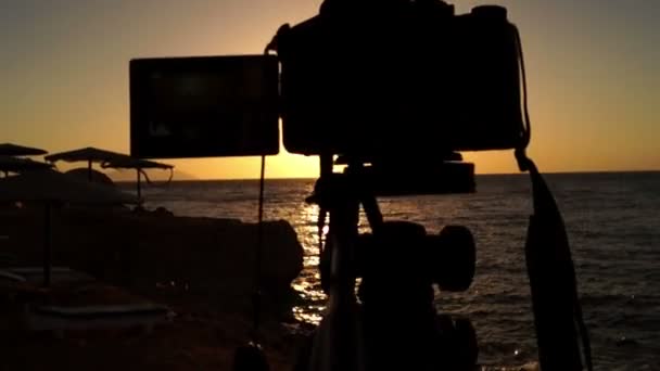 Professionell kamera på stativ står vid solnedgången på stranden i havet. — Stockvideo