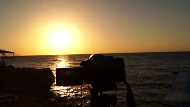 Câmera profissional no tripé fica ao pôr do sol na praia do mar . — Vídeo de Stock