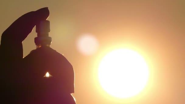 На повітряній кулі з духи в людини рукою красиво розсіює крапель на фоні сонця крупним планом — стокове відео