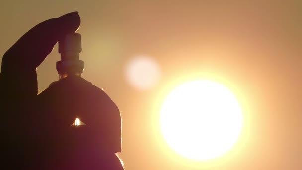 Un globo con perfume en la mano de una persona dispersa maravillosamente gotas en el fondo del sol, primer plano — Vídeos de Stock