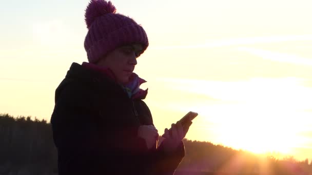 Красива жінка у віці дивиться на інформацію на смартфоні і посмішки, на відкритому повітрі під час заходу сонця — стокове відео