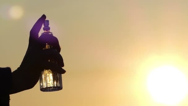 Die Hand hält eine Flasche Parfüm und streut, die Parfümtröpfchen sind schön in der Luft aufgelöst — Stockvideo