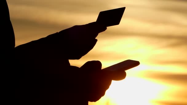 Een persoon controleert het saldo van de creditcard op de telefoon, het silhouet van de kaart en de telefoon is zichtbaar. — Stockvideo