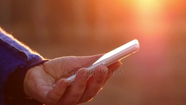 Die Frau benutzt ein Smartphone, Daumen durch die Informationen auf dem Touchscreen, nur ihre Hände sind auf einem schönen verschwommenen Hintergrund zu sehen — Stockvideo