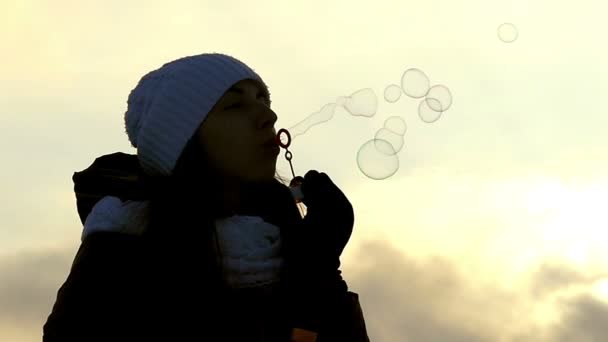 La ragazza in un cappello gonfia colorate bolle di sapone all'aperto in slow motion, la sua silhouette è visibile — Video Stock