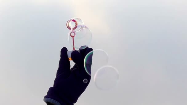 A mão na luva segura uma varinha para bolhas de sabão, movimentos e sob a influência do vento as bolhas são infladas em câmera lenta — Vídeo de Stock