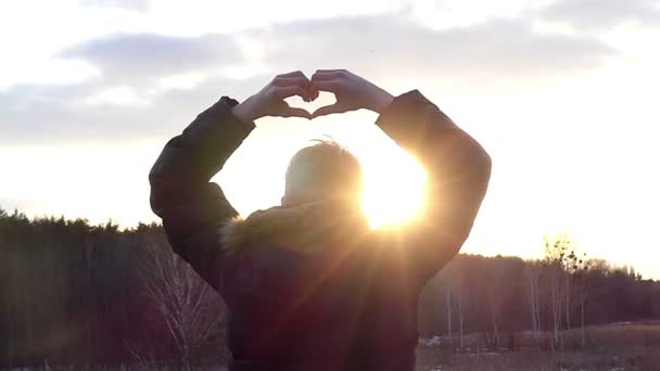 Il ragazzo con la schiena alla macchina fotografica tiene le mani nella forma del cuore sullo sfondo del cielo soleggiato in slow motion — Video Stock