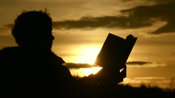 Silhouette eines Jungen mit langen Wimpern liest ein Buch im Freien bei goldenem Sonnenuntergang in Zeitlupe — Stockvideo