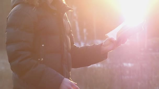 Um jovem iluminado com raios de sol dourados detém um livro e gesticulados com uma mão em movimento lento — Vídeo de Stock