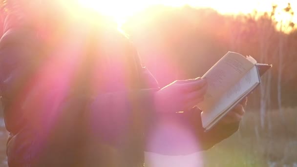Bir kişi ağır çekimde altın güneş ışığı ile aydınlatılan kitabın sayfalarını çevirir — Stok video