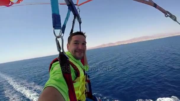 Der Fallschirm mit einem jungen Mann wird an einem sonnigen Tag von einem modernen Motorboot gezogen — Stockvideo