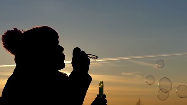 Silhouette einer Frau mit Hut Nahaufnahme bläst Seifenblasen auf dem Hintergrund des schönen Himmels in Zeitlupe auf — Stockvideo