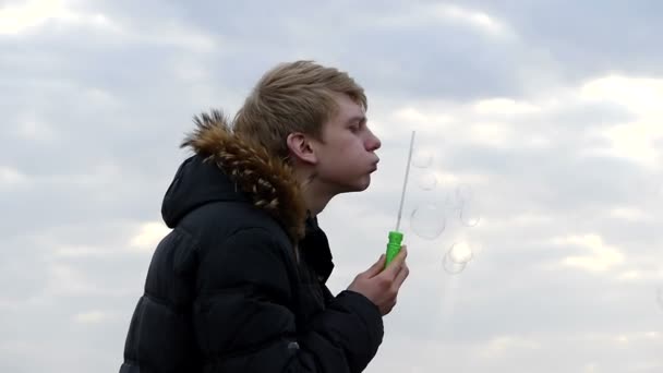 Mladý muž je dělat mýdlové bubliny s speciální zelené Stick v zatažené počasí — Stock video