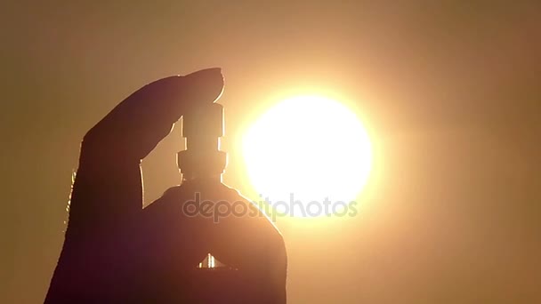 La mano femenina sostiene el perfume y rocía el líquido sobre el fondo de un cielo dorado — Vídeos de Stock